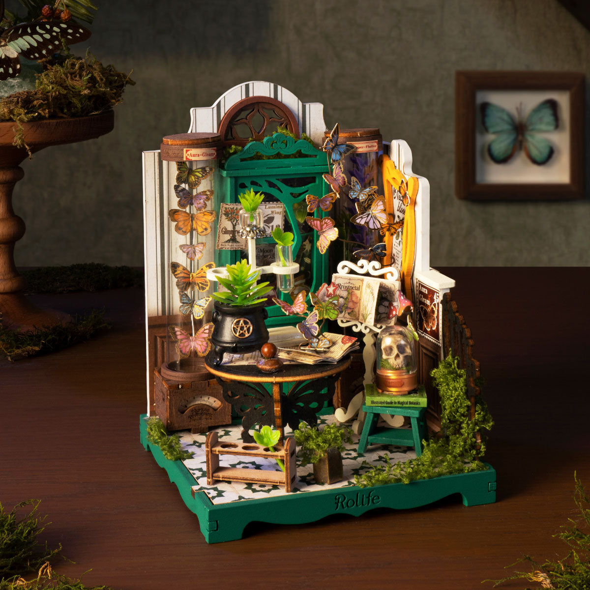 Rolife Potions Workshop miniature displayed on a desk with butterflies, green apothecary cabinet, cauldron, skull dome and warm moody lighting