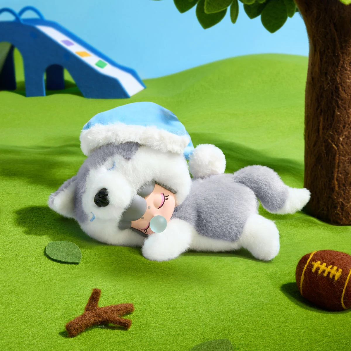 Grey-and-white Nanci Puppy Club Husky plush doll wearing a pale blue nightcap and lying beneath a miniature tree, with a blue slide, twig and toy football nearby.