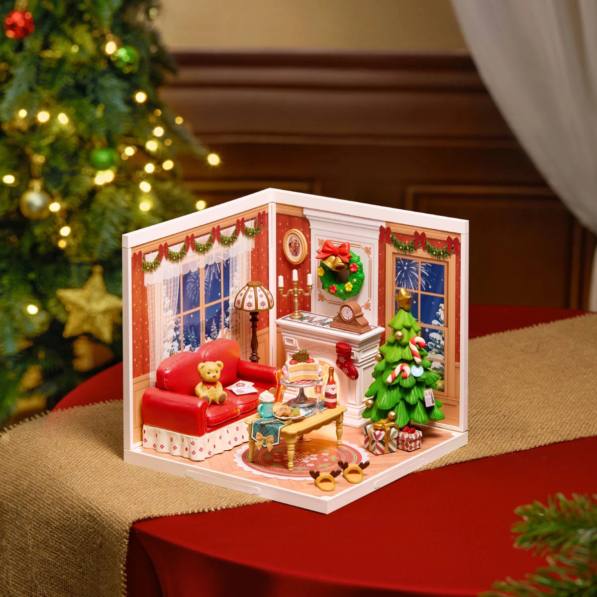 Rolife Twinkling Christmas Eve DIY Miniature House DWZ03 Rolife miniature Christmas living room diorama on a red table runner, showing red sofa, fireplace, Christmas tree and lit windows.
