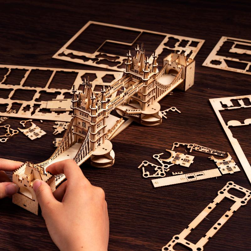 Hands assembling the Rolife Tower Bridge TG412 wooden puzzle from board pieces